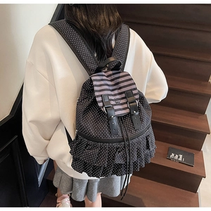 Detailed back view of a black polka dot backpack with ruffle trim on wooden stairs