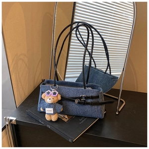 Detailed view of denim baguette bag with leather strap and plush bear keychain