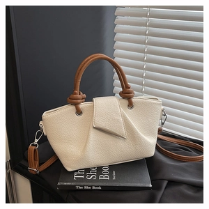 Detail of lychee textured cream tote bag with twisted brown leather handle and silver hardware