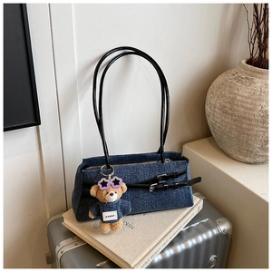 Detailed denim texture of the blue shoulder bag with black straps and bear charm