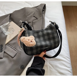 Detail of checkered underarm bag featuring plush bear charm and decorative silk scarf