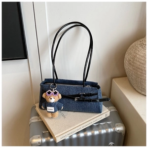 Close-up of denim shoulder bag with bear pendant on a vintage silver suitcase