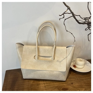 Detail of a cream-colored leather tote bag featuring unique cylindrical long handles