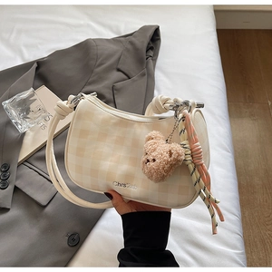 Detail of checkered underarm bag featuring a plush bear charm and woven decorative rope