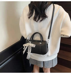 Detail of black pebbled leather Boston bag featuring a white lace and pearl bow charm