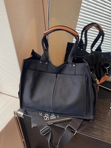 Black canvas tote bag with brown leather handles and adjustable shoulder strap