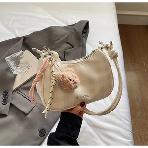 Close-up of beige checkerboard hobo bag with teddy bear charm and knotted strap detail