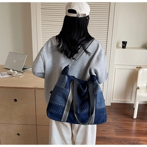 Detail of large denim tote bag featuring white contrast stitching and striped woven handle