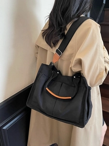 Minimalist black canvas tote bag with brown leather handles worn with a beige trench coat