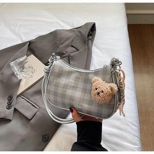 Detail of grey checkered underarm bag with plush bear charm and silk scarf decoration