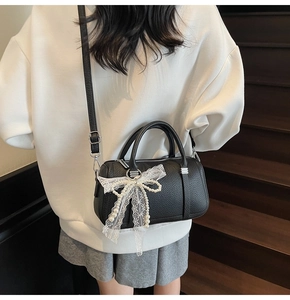 Detail of black pebbled leather pillow bag featuring a lace bow and pearl pendant