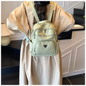 Detail of pistachio green leather backpack featuring multiple zippers and metallic logo