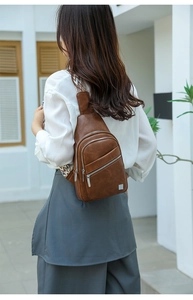 Brown faux leather sling bag with geometric woven strap worn by a model in soft daylight