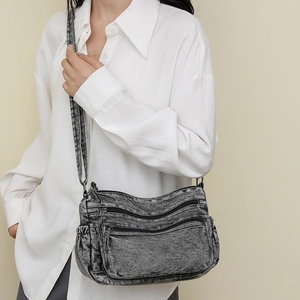 Détail du sac bandoulière en denim gris avec plusieurs poches zippées sur modèle