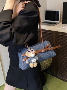 Blue denim baguette bag with brown leather handles and a teddy bear charm detail