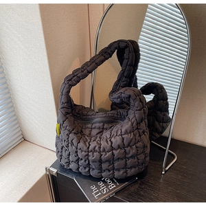 Detail of black quilted puffer bag with crossbody strap on a minimalist wooden surface