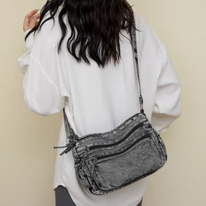 Détail d'un sac bandoulière en denim gris avec fermetures éclair et poches multiples