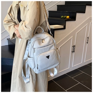 Detail of light grey pebbled leather backpack with triangular metal logo and zippers