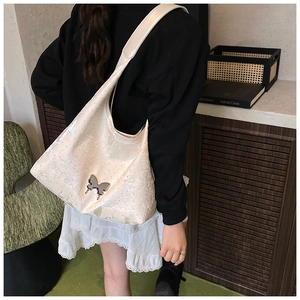 Detail einer cremeweißen Hobo-Tasche aus glänzendem Jacquard mit silbernem Schmetterling