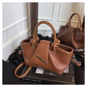 Detail of brown lychee grain leather tote with knotted handle and gold metal clasp hardware