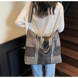 Detail of a large denim patchwork tote bag with striped straps shown on a wooden staircase