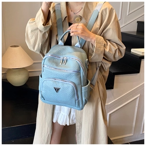 Detail of light blue textured leather backpack with multi-zipper pockets and silver plate