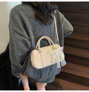 Close-up of off-white lychee grain boston bag with elegant lace bow and pearl charm
