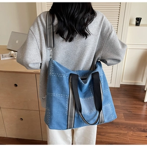 Blue denim tote bag with contrast white grid stitching and striped handles on a model