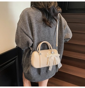 Close-up of beige leather bowling bag with lace bow and pearl pendant on a model