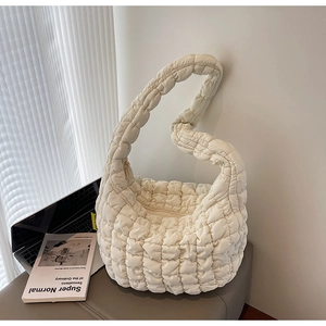 Detail of a beige quilted cloud bag with padded puffer design on a grey soft stool