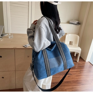 Detail of blue denim tote bag featuring white quilted stitching and wide striped strap