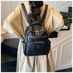 Detail of black pebbled leather backpack with silver zippers and metal logo on beige coat