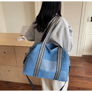 Detail of blue denim tote bag showing white stitching pattern and striped handle straps