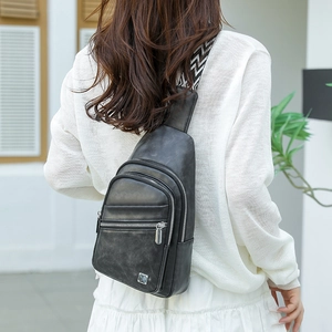 Detail of black faux leather chest bag with patterned strap and silver metal zippers