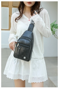 Close-up of black chest bag featuring dual zippers and a wave-patterned woven strap