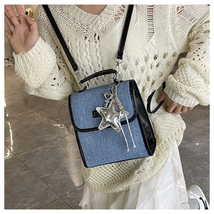Detail of blue denim crossbody bag with silver star and heart charms on a beige top