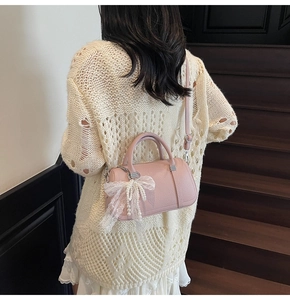 Pink cylinder bowling bag with lace bow and pearl charm shown on model in warm interior
