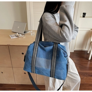 Detail of blue denim patchwork tote bag showing contrast stitching and striped web handles