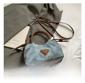 Detail of light blue denim pleated bag with brown leather handles and triangle logo