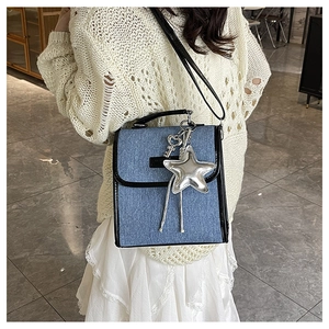 Detailed view of blue denim shoulder bag with silver star charm worn by a model
