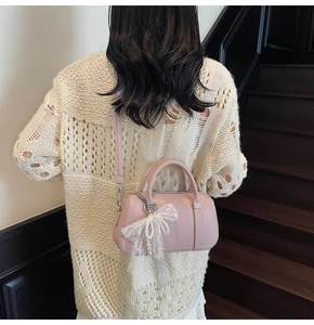Pink lychee grain leather pillow bag with lace pearl bow charm worn by a model