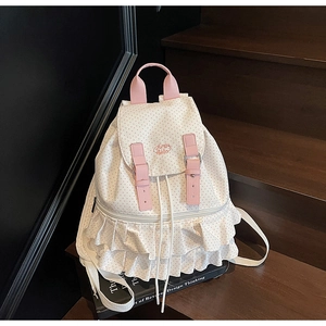 Detailed view of white polka dot backpack with ruffle trim on dark wooden stairs