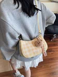 Stylish yellow checkerboard shoulder bag with plush bear charm and knot strap detail