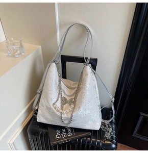 Détail du sac cabas blanc jacquard papillon avec perles et chaîne sur une valise