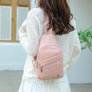 Detail of light pink crossbody chest bag showing decorative woven strap and multi-zipper pockets