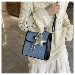 Close-up of denim crossbody bag with black trim and a silver star charm accessory
