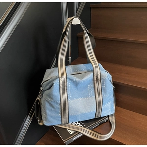Detail view of denim tote bag with contrast stitching and striped woven handle on display