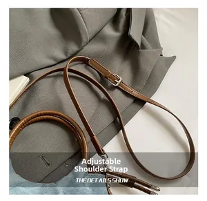 Detail of light blue denim handbag with brown leather adjustable strap and silver metal buckle