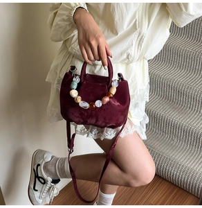 Détail du sac seau en velours bordeaux avec poignée décorative en perles de résine