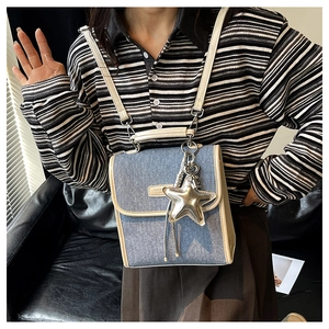 Detail of blue denim shoulder bag featuring star pendant and cream leather trim edges